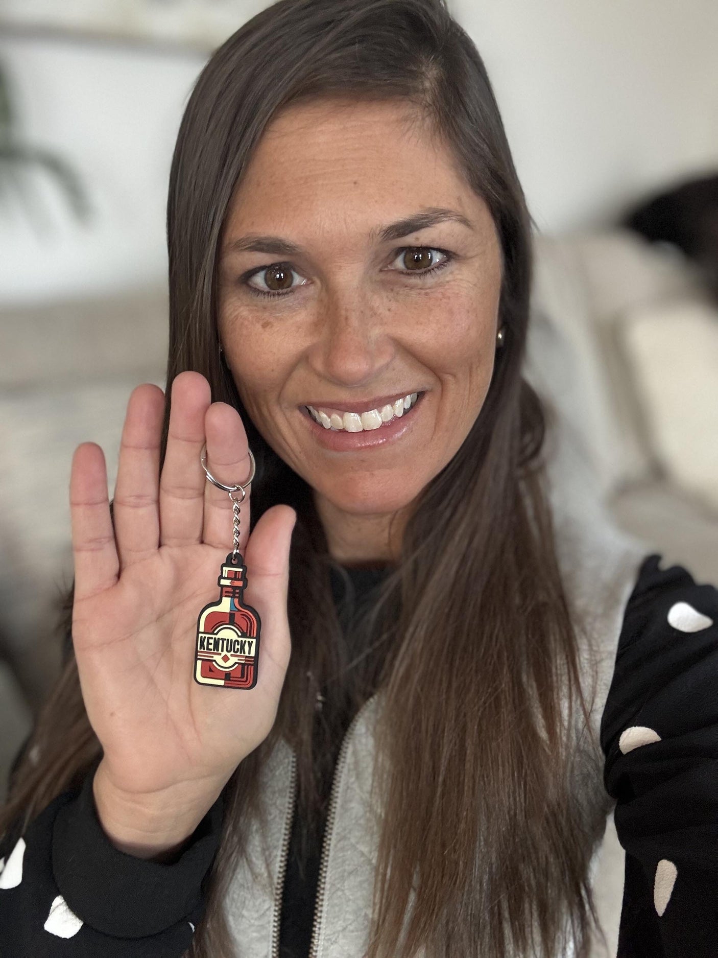 Kentucky keychain held in a woman's hand, featuring a bottle design with red and yellow colors.