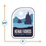 Kenai Fjords National Park sticker featuring mountains, water, and a sun in blue and black colors, measuring 2.75 by 2 inc...