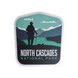 North Cascades National Park sticker featuring a hiker silhouette against mountains and a river in green and blue tones.