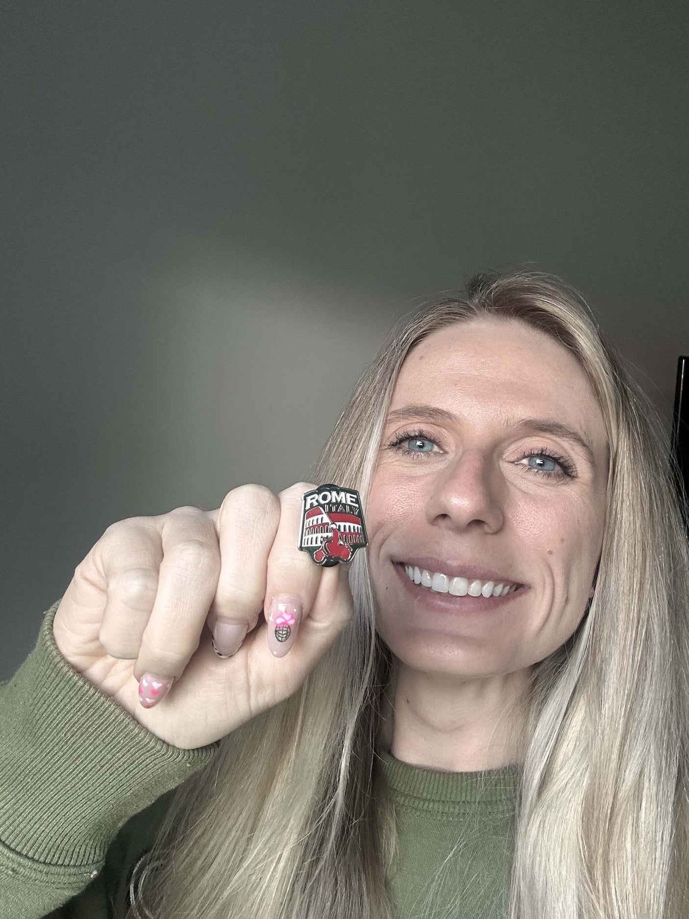Enamel pin featuring "Rome" text with a red and black design, held by a person with long blonde hair.