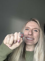 Enamel pin featuring "Rome" text with a red and black design, held by a person with long blonde hair.
