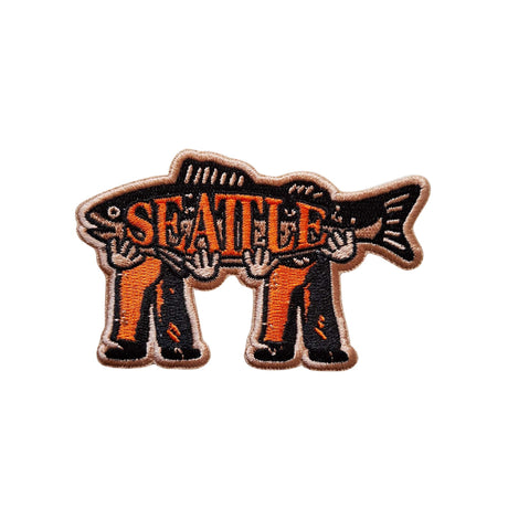 Seattle patch featuring a fish design held by two figures, with orange and black embroidery on a beige background.