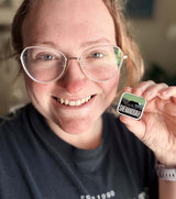 Shenandoah National Park enamel pin held by a person, featuring green and black colors with the word "SHENANDOAH.