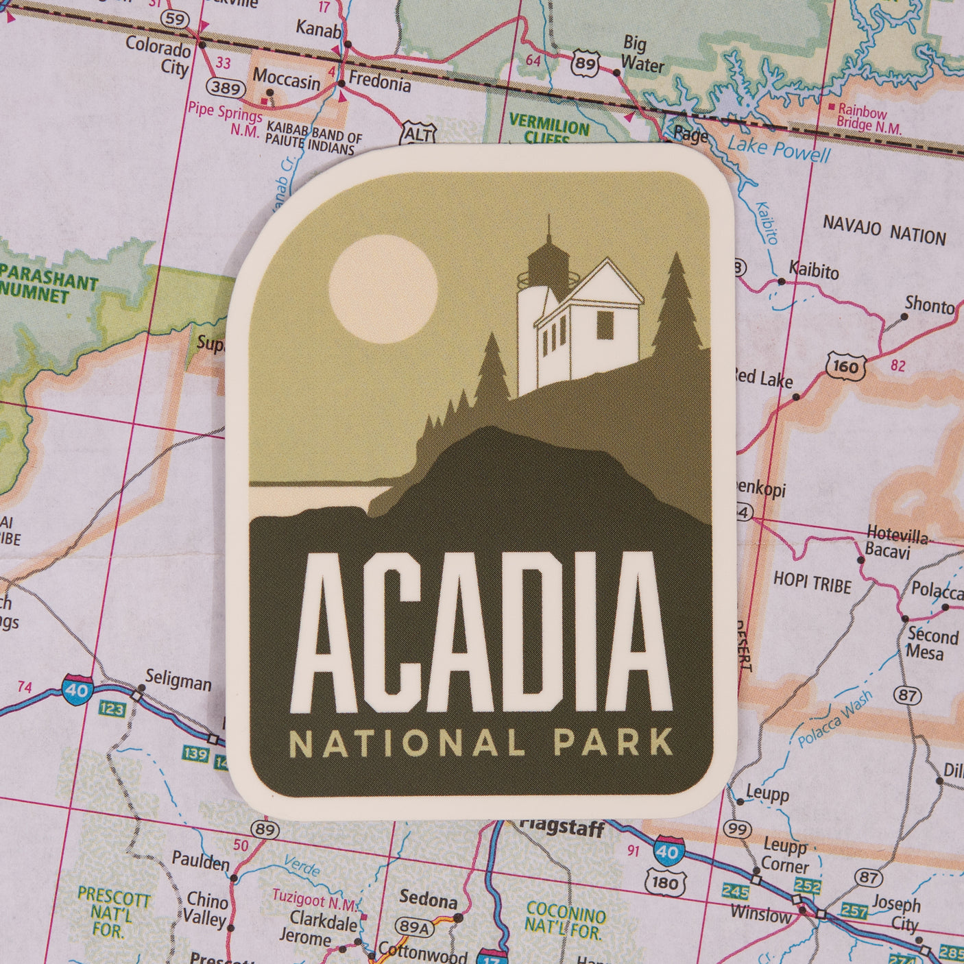 Acadia National Park sticker featuring a lighthouse and sun on a map background.