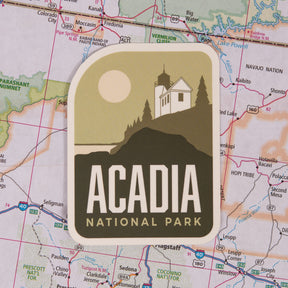 Acadia National Park sticker featuring a lighthouse and sun on a map background.