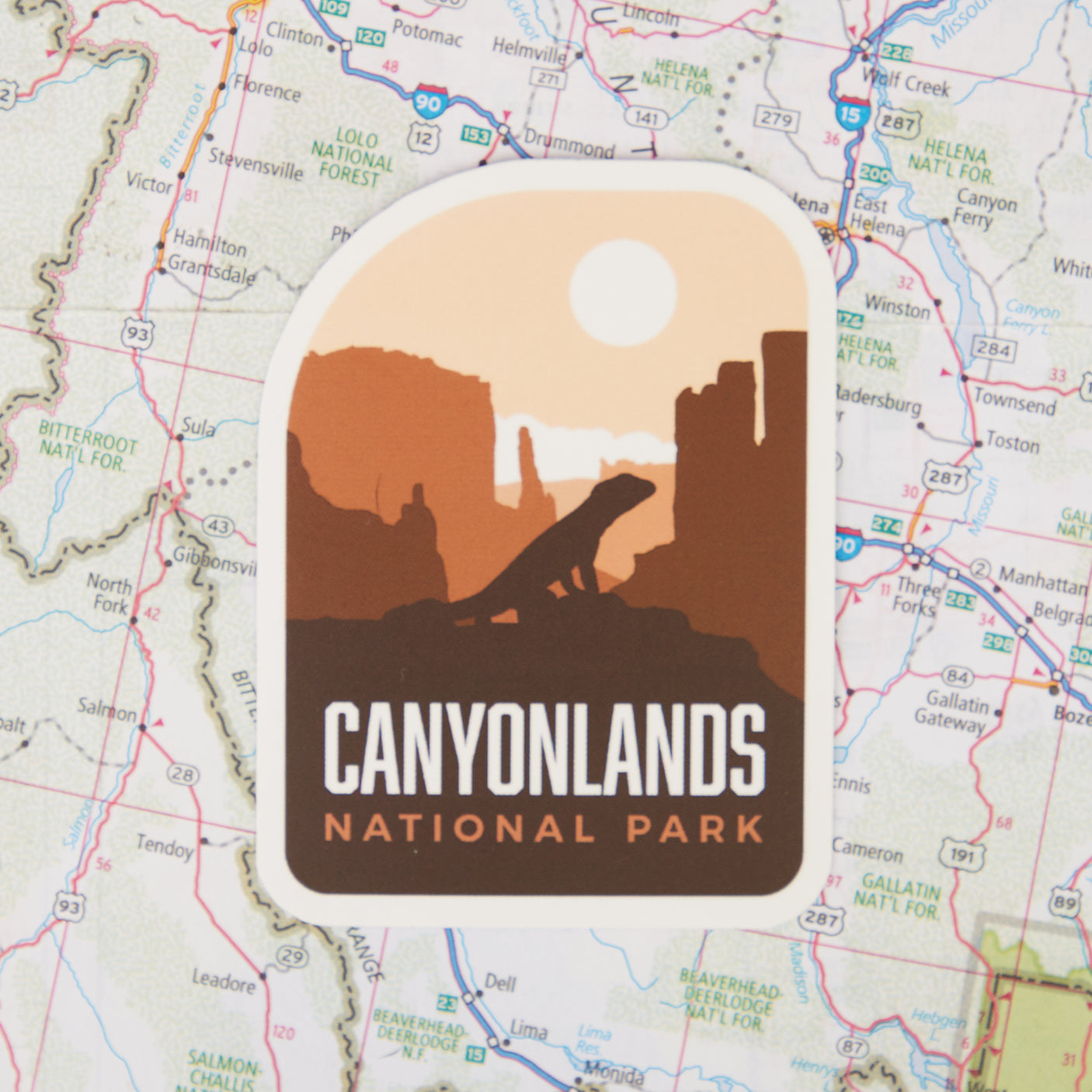 Canyonlands National Park sticker featuring a silhouette of rock formations and a lizard against an orange background.